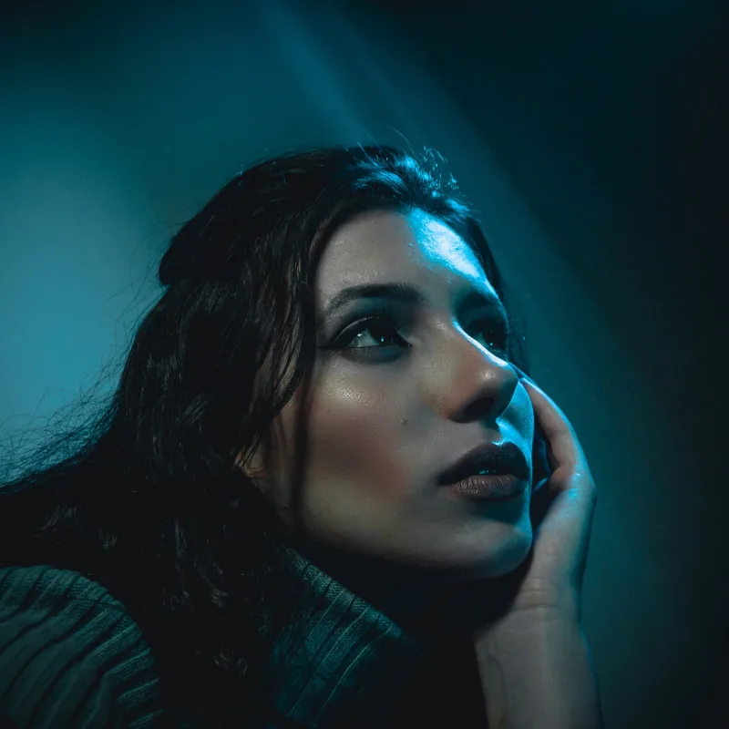 A portrait lit in deep teal, the subject looking toward the light